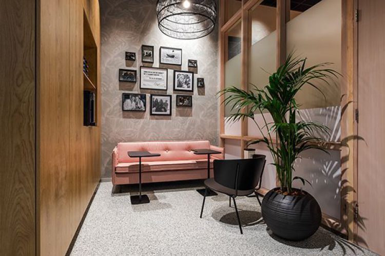 Ontspanningsruimte met roze bank, fotowand en natuurlijke verlichting – sfeervolle en impactvolle invulling van een rustplek binnen de werkplek.